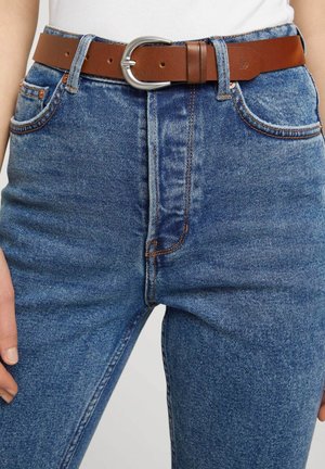 Brązowy skórzany pasek z srebrną owalną klamrą, zestawiony z niebieskimi dżinsami o wysokim stanie z klasycznym pięciopocketowym krojem i wyblakłą strukturą.