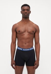 Schwarze Boxer-Briefs mit einem breiten blauen Bund, auf dem "BJÖRN BORG" in weißer Schrift steht. Glattes Material mit einem engen Sitz, das die Form und das Design betont.