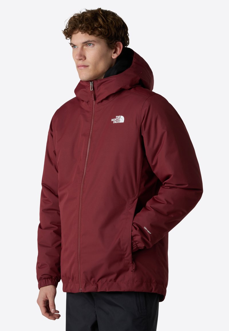 Giacca isolata color mogano con zip frontale, cappuccio e polsini elasticizzati. Presenta il logo sul petto e tasche laterali, realizzata in materiale resistente all'acqua.