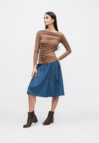 Pruun pika varrukaga ülaosa, millel on kortsuline disain ja nööpdetailid, kombineeritud teksast A-lõikelise seelikuga, millel on külgkinnitus ja pruunide pahkluu saapadega.