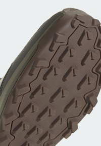 Gros plan d'une semelle de chaussure marron avec un motif de bande de roulement texturé triangulaire et rectangulaire pour une adhérence extérieure.