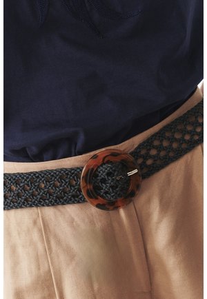 Black woven belt with a circular tortoiseshell buckle, worn over a light brown garment, showcasing intricate knit texture and design.