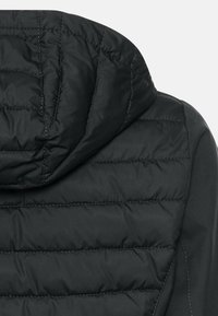 Zwarte pufferjack met capuchon, voorzien van gestikte quiltnaden, een gladde afwerking en een afgeronde vorm. Kenmerken zijn een slank ontwerp en een subtiele glans.