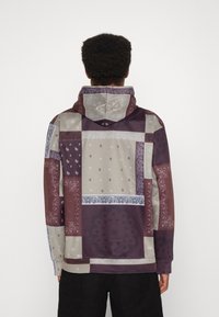 Mikina s kapucí se vzorem patchwork v odstínech vínové, šedé a béžové s propracovanými paisley vzory. Obsahuje stahovací kapuci.