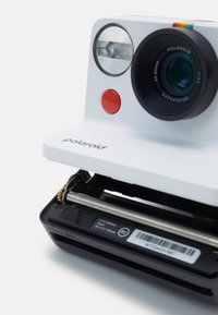 Polaroid camera with a glossy white body, a round lens, red button, and flash. Bottom section shows battery compartment with details.