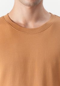 T-shirt à manches courtes et col rond dans une teinte marron unie. Fabriqué dans un tissu lisse et doux, avec une coupe régulière et sans motifs ni accents visibles.