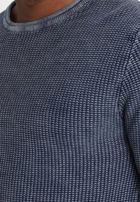 Pull en maille texturée bleu marine avec un col rond, présentant un motif subtil et des poignets côtelés, fabriqué dans un matériau doux et extensible.