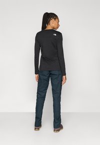 Langermet svart skjorte med en glatt tekstur og en logo på øvre del av ryggen, kombinert med mørkeblå cargobukser med sidelommer.