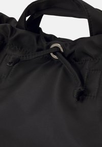 Sac en tissu noir avec une poignée cousue et un cordon de serrage passé à travers un œillet en argent à la fermeture supérieure.