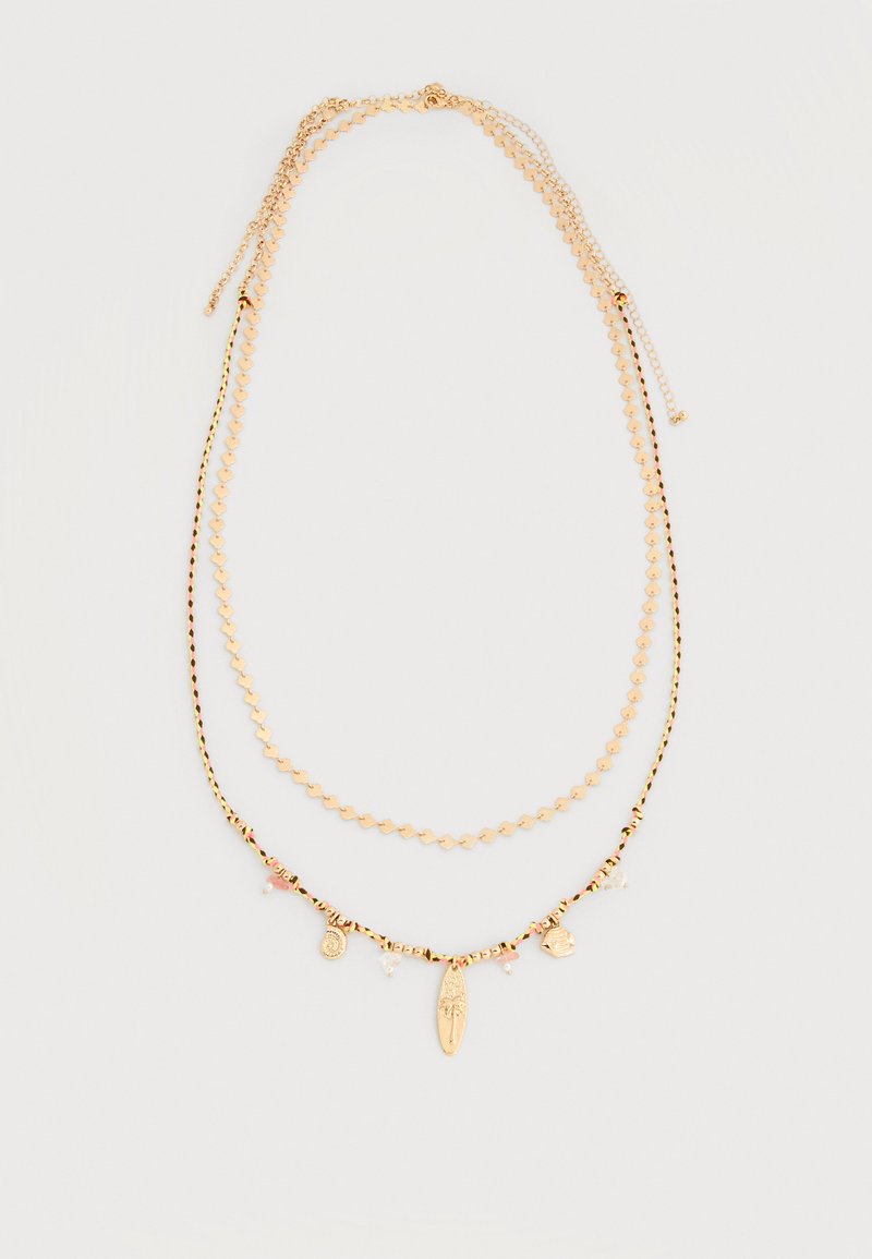 Deux colliers superposés en ton or, l'un avec de petits maillons en forme de cœur, l'autre avec un cordon tressé noir et or orné de breloques pendantes.