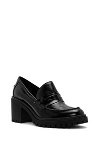 Mocassin à talon en cuir noir avec semelle crantée épaisse et bout arrondi, incliné pour montrer l'avant et le côté extérieur.