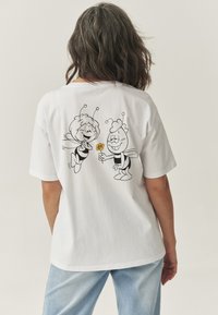 Hvid bomuld t-shirt med en sort linjeillustration af to tegneseriebi på bagsiden, hvoraf den ene holder en gul blomst.