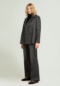 Grijze visgraat dubbelgeknoopte jas met een gestructureerde kraag, gecombineerd met donkere jeans met wijde pijpen en zwarte platte schoenen. Glad oppervlak en een getailleerde pasvorm.