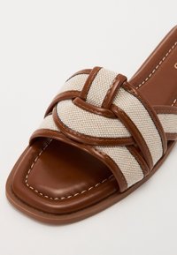 Brune lædersandaler med glidesål og et vævet beige stofbånd, der har et knyttet design og cremefarvet syninger langs kanterne.