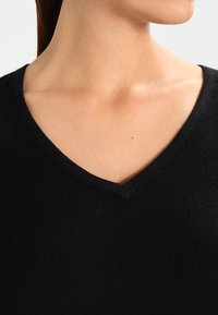 Czarny sweter dziany z dekoltem w szpic, charakteryzujący się miękką teksturą i minimalistycznymi szwami wokół dekoltu i ramion.