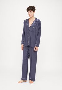 Navy striped pajama set with long sleeves and pants, featuring a button-down shirt, pocket, and contrast piping around the collar and cuffs.