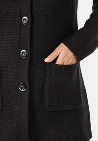 Schwarze Strickjacke mit strukturiertem Strick, silbernen Knöpfen und zwei Vorder-Taschen. Die Ärmel sind gerippt und bieten eine enge Passform.