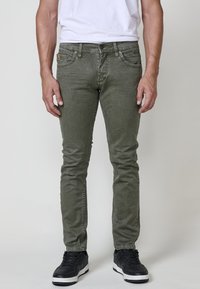 Olive zelene skinny jeans iz bombažne mešanice, s sprednjimi žepi, zadrgo in črnimi supergami z belimi podplati.