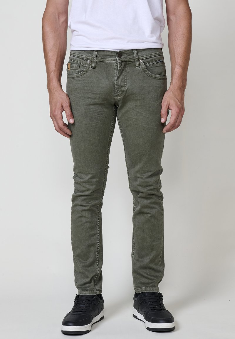 Olive zelene skinny jeans iz bombažne mešanice, s sprednjimi žepi, zadrgo in črnimi supergami z belimi podplati.