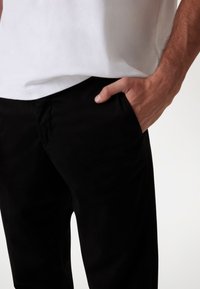 Sorte bomuldsbukser med sidelommer, flad frontdesign og slim fit. Båret med en ensfarvet hvid skjorte. Glat tekstur, ingen mønstre.