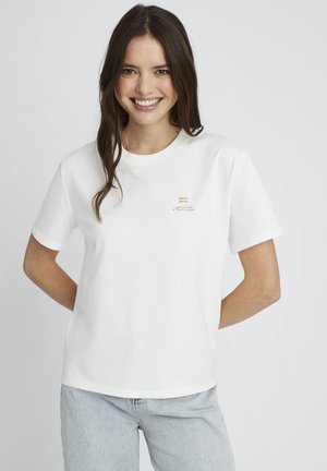 T-shirt en coton blanc à manches courtes, décolleté rond et détail de logo doré sur le devant. Associé à un jean bleu clair.