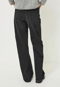 Jeans neri a gamba larga in denim, con due tasche posteriori, cuciture bianche a contrasto e un taglio dritto, visti da dietro.