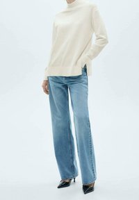 Pull crème à col roulé décontracté, associé à un jean en denim bleu clair à jambes larges. Des escarpins noirs à bout pointu complètent la tenue.