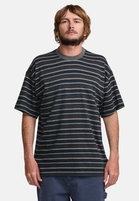 Striped short-sleeve t-shirt in navy with thin cream and gray stripes, featuring a round neckline and loose fit. Soft fabric texture.