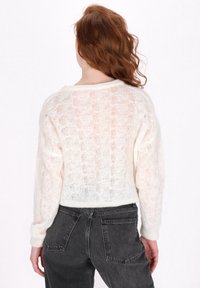 Weißer, kurz geschnittener Pullover mit einem lockeren Strickmuster und rundem Halsausschnitt. Hat lange Ärmel und gerippte Bündchen. Wird mit dunklen, engen Jeans getragen.