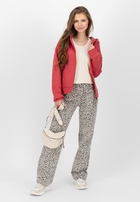 Felpa rossa con zip, top beige, pantaloni a gamba larga con stampa animale, borsa crema e sneakers beige. Texture morbide e motivi contrastanti.