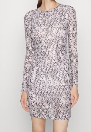 Žena v dlouhých rukávech, těsně přiléhajících mini šatech s opakujícím se vzorem písmen "CHOU" v jemně růžové a černé barvě.