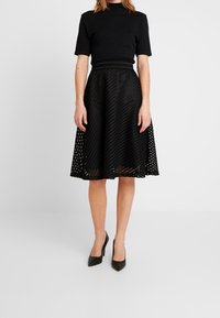 Schwarzes Kleid mit einem eng anliegenden Oberteil mit kurzen Ärmeln und einem ausgestellten Rock aus geschichtetem, gemustertem Stoff, knielang.