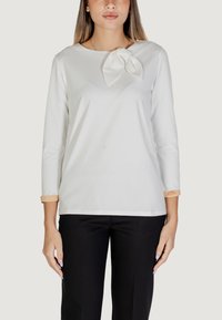 Maglietta bianca a maniche lunghe con dettaglio a fiocco sul collo, con accenti beige a contrasto sulle maniche. Tessuto morbido e liscio.