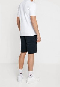 Bílá krátkosrstá tričko, námořnické šortky, bílé tenisky a vzorované ponožky; minimalistický design, těsný střih, bavlněný materiál.