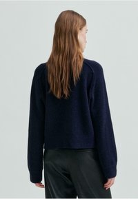 Marineblå genser med teksturstrikk, forkortet kant og senkede skuldre, sammen med svarte bukser. Mykt stoff, avslappet passform.