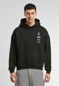 Zwarte hoodie met een buidelzak, voorzien van witte logo-opdrukken op de borst. Gemaakt van zacht materiaal met ribgebreide manchetten en onderkant.