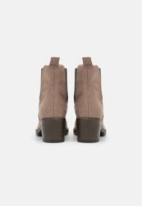 Paire de bottines en daim marron avec talons carrés en bois foncé vues de dos sur un fond blanc.