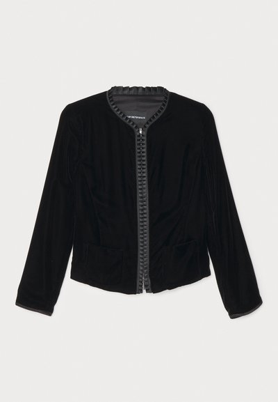 Chaqueta de terciopelo negro con cremallera, con un cuello con volantes, dos bolsillos frontales y mangas largas. Textura suave con un diseño ajustado.