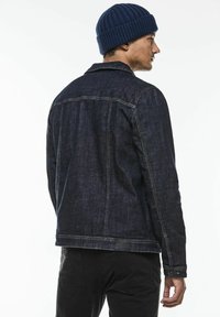 Tmavě modrá džínová bunda s klasickým designem, viditelným šitím a bočními kapsami, doplněná o pletenou námořnickou čepici.