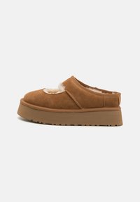 Brown suede slip-on shoes with a fluffy cream interior. Features a rounded toe and thick brown platform sole with textured tread.