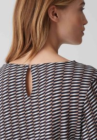 Blouse met knoopsluiting, voorzien van een geometrisch patroon in wit, marineblauw en bruin, met een keyhole-detail aan de achterkant en een zachte textuur.