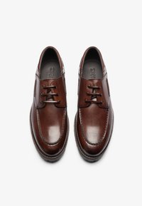 Zapatos de piel marrón con un acabado suave, punta redondeada, diseño con cordones y detalles de costura en contraste. Logo grabado visible en la plantilla.
