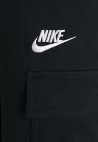 Svarta cargobyxor i tyg med en broderad vit Nike-logga. Har en sidoficka och texturerade sömmar.