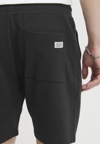 Black waffle-textured shorts with a back pocket and a small label. The fabric appears lightweight and breathable, designed for casual wear.
