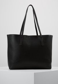Bolso tote de cuero negro texturizado con dos asas largas para el hombro, exhibido en un pedestal blanco contra un fondo claro y liso.