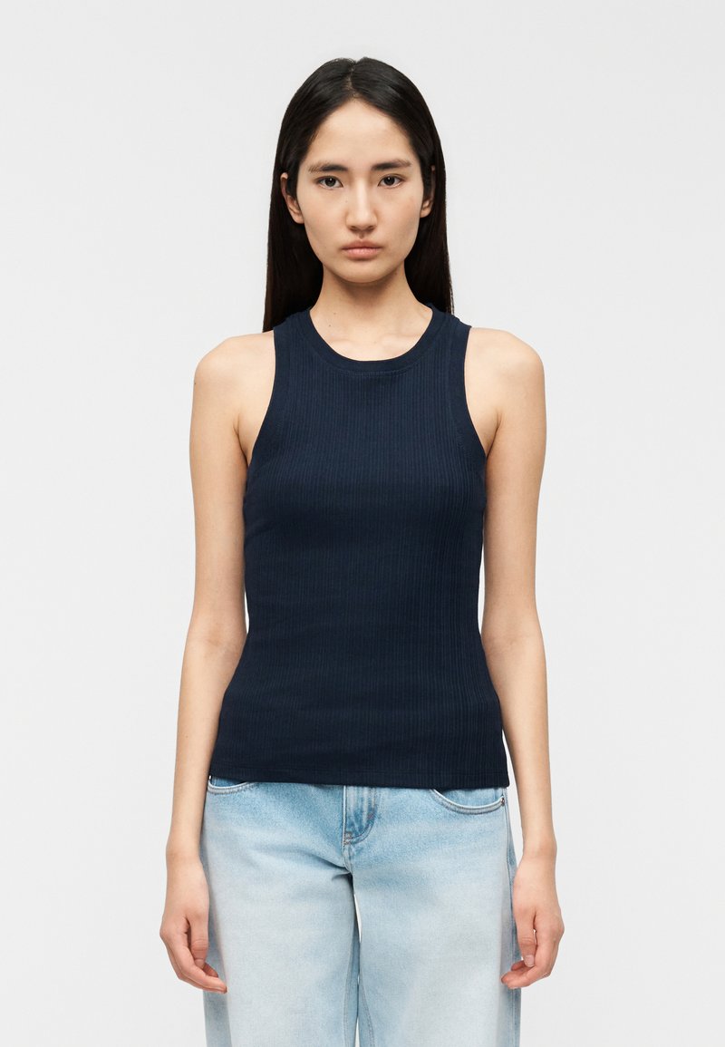 Μπλε ναυτικό ριμπ τοπ με στρογγυλό λαιμό και αμάνικο σχέδιο, σε συνδυασμό με ανοιχτόχρωμο γαλάζιο τζιν ψηλόμεσο.