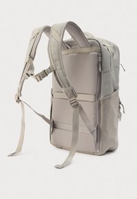 Γκρι υφασμάτινο σακίδιο πλάτης με ρυθμιζόμενους ιμάντες, τσέπες με φερμουάρ και υφή στο φινίρισμα. Πλευρική τσέπη από δίχτυ και ενισχυμένη βάση.