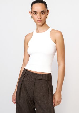 Biały prążkowany crop top z wysokim dekoltem, zestawiony z brązowymi spodniami o wysokim stanie i fakturze. Gładki materiał, bez rękawów.