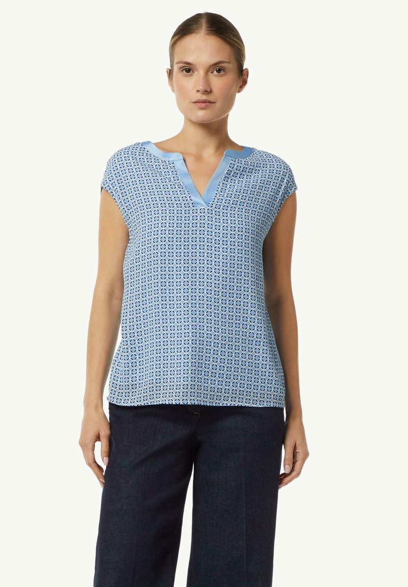 Hellbluse mit geometrischem Muster, V-Ausschnitt und kurzen Ärmeln. Weicher, leichter Stoff mit glatter Textur.