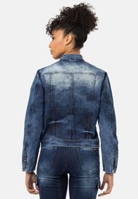 Denimjacke mit einem abgestuften blauen Waschung, mit Kragen, tailliertem Schnitt und detaillierter Stickerei. Lange Ärmel mit Knopfmanschetten.